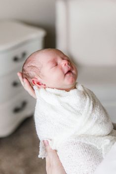 a baby wrapped up in a blanket being held by someone's hand while laying on the floor