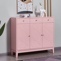 a pink cabinet with an animal statue on top and a painting above it in the corner