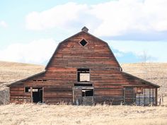 an old barn sits in the middle of a field with no grass or flowers on it