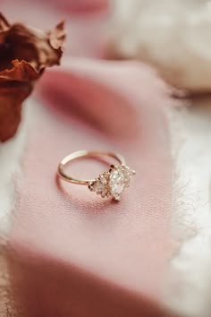 an engagement ring sitting on top of a pink cloth next to a dried rose flower