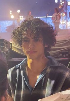 a young man with curly hair sitting in front of a microphone and looking at the camera