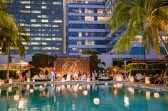 an outdoor pool surrounded by palm trees in front of a tall building with lights on it