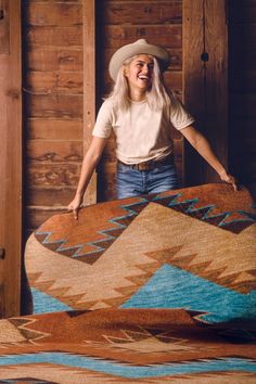 a woman wearing a cowboy hat standing next to a large rug in a wooden cabin