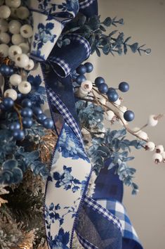 a blue and white christmas tree is decorated with berries, branches, and fabric ribbons