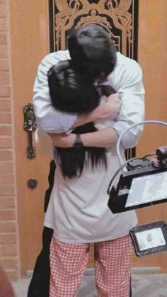 a man and woman hugging each other in front of a door with an electronic device