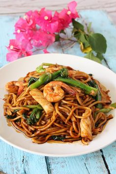 a white plate topped with noodles and shrimp next to chopsticks on a blue wooden table