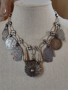 An assemblage of ethnic silver elements featuring a 925 sterling Yemeni amulet with the makers mark, possibly made by a Jewish Bawsani silversmith. I've flanked it with silver Turkmen pendulum shaped pendants, two walking liberty coin pendants from a Navajo squash blossom necklace, and Moroccan Berber Hamsa in two styles. All elements are suspended from triple plated silver chain. Finishes with a silver plated hook. Traditional Medallion Necklace For Collectors, Handmade Amulet Coin Necklace, Artisan Style Medallion Necklaces With Oxidized Finish, Artisan Medallion Necklaces With Oxidized Finish, Artisan Medallion Necklace With Oxidized Finish, Artisan Sterling Silver Necklaces With Oxidized Finish, Vintage Medallion Jewelry For Rituals, Artisan Sterling Silver Necklace With Oxidized Finish, Artisan Oxidized Pendant Jewelry