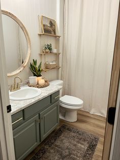 a white toilet sitting next to a bathroom sink under a round mirror on top of a wooden cabinet