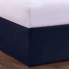 a bed with white and blue sheets on top of wooden flooring in a bedroom