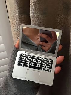 a person holding a laptop computer in their left hand and looking at the screen with a woman's reflection on it