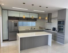 a modern kitchen with stainless steel appliances and marble counter tops, along with pendant lights hanging from the ceiling