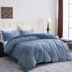 a bed with blue comforter and pillows in a bedroom next to a lamp on a table