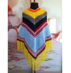 a colorful crocheted ponchle with fringes on display in a room