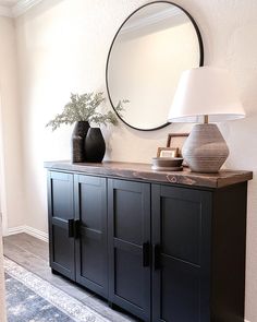 a black cabinet with two vases and a round mirror on the wall above it