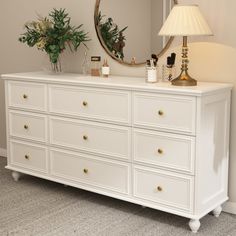 a white dresser sitting next to a mirror and lamp