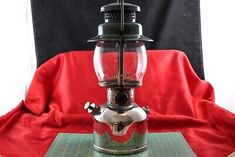 an old fashioned coffee grinder sitting on top of a green cutting board with a red cloth behind it