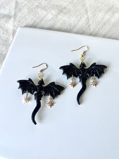 Black dragons made from clay, each dragon with two 18k gold plated north star charms  My earrings  are handmade with polymer clay, an extremely light weight and versatile material. Each individual piece is handcrafted with care and attention, no two are alike. There may be slight variations in colors or shape and potential imperfections. Choose your hardware made from gold* or silver and choose between ball posts, lever back huggie hoops, hooks or hoops. Hardware used may vary from photos.  *Gol Dragon Clay, Earrings Dragon, Black Dragons, Fantasy Earrings, Celestial Earrings, Dragon Earrings, Black Dragon, North Star, Star Charms