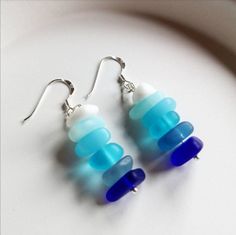 two blue and white glass beads are hanging from silver earwires on a plate