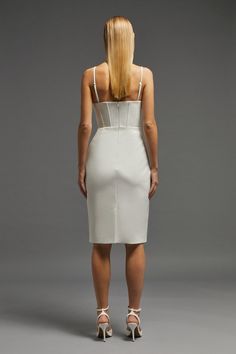 the back of a woman wearing a white dress with straps and heels on her feet