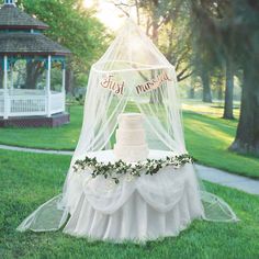 a white wedding cake sitting on top of a lush green field next to a gazebo