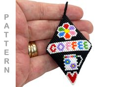 a hand holding a small beaded ornament in the shape of a triangle