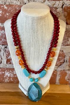 Agate Ambrosia Statement Necklace Genuine Scarlet Jade Genuine Amber Resin Genuine Agate Genuine Turquoise Magnesite Gold-Tone Metal Lobster Claw Clasp Crafted and Finished by Hand Approximate Measurements: Length- 17" + 2" Extender; Pendant is 2.25" in Length and 1.5" in Width Adorn yourself with the mesmerizing beauty of the Agate Ambrosia Statement Necklace! Crafted from genuine Scarlet Jade, Amber Resin, Agate, and Turquoise Magnesite, each stone is lovingly encased in a gold-tone metal sett Red Agate Jewelry With Natural Stones, Double Strand Jewelry With Gemstone Accents For Gift, Faceted Agate Beads Long Necklace, Bohemian Red Jewelry With Gemstone Accents, Turquoise Agate Faceted Bead Necklaces, Turquoise Agate Faceted Beads Necklace, Turquoise Agate Necklace With Faceted Beads, Double Strand Agate Jewelry With Natural Stones, Turquoise Agate Gemstone Beaded Necklaces