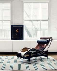 a chair sitting on top of a blue rug in front of a window and a painting