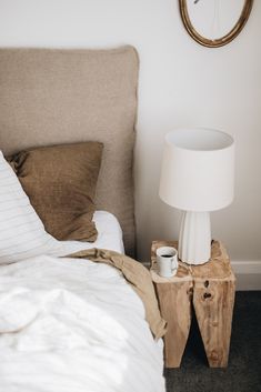 a white lamp sitting on top of a wooden table next to a bed