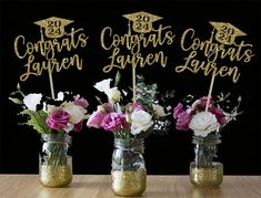 three mason jars filled with flowers and topped with gold glitter graduation cap cake toppers