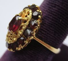 This ring looks so regal! The deep red garnets against the rich colored 18k gold compliment each other beautifully. Dating from the early 1900's-40's and hallmarked in the interior 750 and 176AAL. Has been tested to ensure the golds purity. Rings size is 6 1/2 and is ready to be worn and admired! The halo setting measures 11/16 by 7/16 of an inch. Stones are all held securely in place. Center garnet measures 6.12mm by 4.25mm. Some stones have light surface wear as to be expected with a ring of s Elegant Garnet Ruby Ring Stamped 14k, Heirloom Yellow Gold Garnet Jewelry, Heirloom Gold Garnet Rings, Luxury Garnet Rings Hallmarked, Gold Garnet Multi-stone Ring, Yellow Gold Garnet Multi-stone Ring, Luxury Hallmarked Garnet Rings, Multi-stone Garnet Ring In Yellow Gold, Elegant Red Rings For Ceremonial Occasions