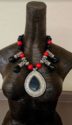 A vintage black onyx and silver tone metal ethnic pendant is featured in this black, red and silver unisex tribal statement necklace. The primary pendant measures 4" x 3" while the black onyx or black agate teardrops measure 2.5" x 1". Each teardrop has inlaid turquoise and coral. The remainder of the necklace includes red magnesite, silver tone tribal bi-cones, silver tone daisy spacers, black onyx beads, black faceted crystals, purple jade and silver tone metal spacers. Adjusts from 20-23" and Traditional Black Beaded Necklaces With Natural Stones, Traditional Teardrop Large Pendant Necklace, Traditional Black Necklaces With Silver Beads, Traditional Black Necklaces With Natural Stones, Traditional Black Jewelry With Silver Beads, Traditional Black Necklace With Silver Beads, Traditional Teardrop Pendant Necklace, Black Teardrop Bohemian Jewelry, Traditional Black Onyx Necklace