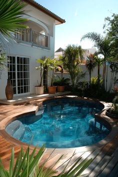 a small pool in the middle of a wooden deck next to a white house and palm trees