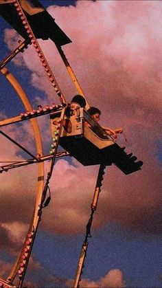 a man riding on top of a ferris wheel under a cloudy blue and pink sky