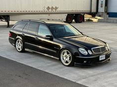 a black mercedes benz wagon parked in front of a semi - truck on the road