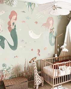 a baby's room with a crib, bed and wallpaper featuring mermaids