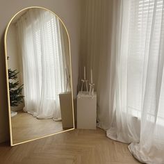 a mirror sitting on top of a wooden floor next to a christmas tree in front of a window