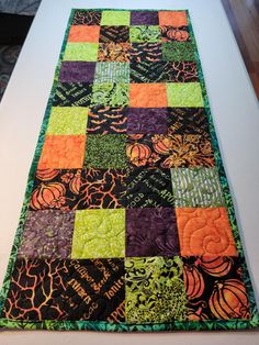 a quilted table runner with pumpkins and leaves on the top in black, green, orange, and purple