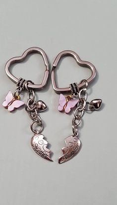 two heart shaped key chains with charms attached to them on a gray surface, one has a pink ribbon and the other is silver