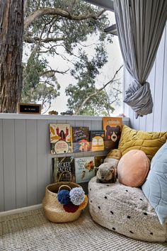 there is a bed with pillows and books on the floor next to a basket full of books