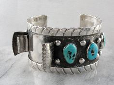 This is a watch band cuff bracelet, intended for a gentleman, and made in the American Southwest at some time around 1970 or so. The style is interesting, a slightly off set motif that allows the watch to be fully visible without turning the wrist. These turquoise nuggets are lovely, bright blue with wonderful deep silver matrix. Metal: Sterling Silver Gem: 4 Turquoise Nuggets Gem Measurements: Size and Shape Varies Width: 1 1/1 Inches Inside Diameter: 2 1/2 Inches Vintage Rectangular Watch Band With Bracelet Strap, Vintage Adjustable Cuff Watch, Vintage Cuff Watch Band As Gift, Vintage Cuff Watch, Unique Cuff Bracelet For Formal Occasions, Vintage Wide Band Bracelet For Formal Occasions, Vintage Cuff Bracelet Watch Bands, Vintage Cuff Watch Bands With Bracelet Strap, Unique Collectible Cuff Bracelet