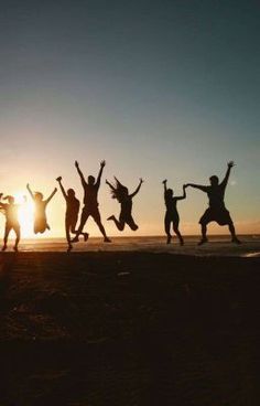 five people jumping in the air on a beach at sunset with their hands up and arms outstretched