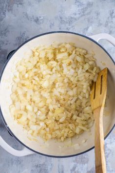 onions being cooked in a pot with a wooden spoon