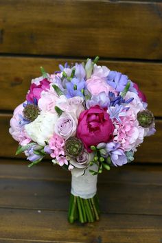 a bridal bouquet with pink, purple and white flowers on a wooden bench in front of a wood paneled wall