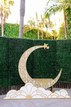 a golden crescent and star sitting on top of a cloud in front of a hedge