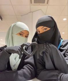 two women dressed in black and grey are sitting down with their heads covered by burkas