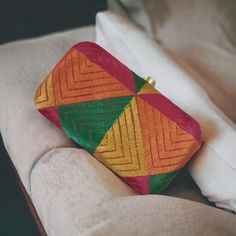 an orange, green and yellow purse sitting on top of a white couch next to a pillow