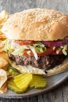 a hamburger with lettuce, tomato and onion on a plate next to chips