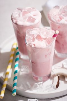 three glasses filled with ice and some straws on a tray next to two bananas