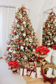 two christmas trees decorated with red, white and gold ornaments in front of a mirror