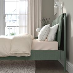 a bed with white pillows and green headboard in front of a window, next to a rug